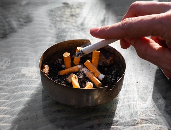 hand tapping cigarette over ashtray and cigarette butts